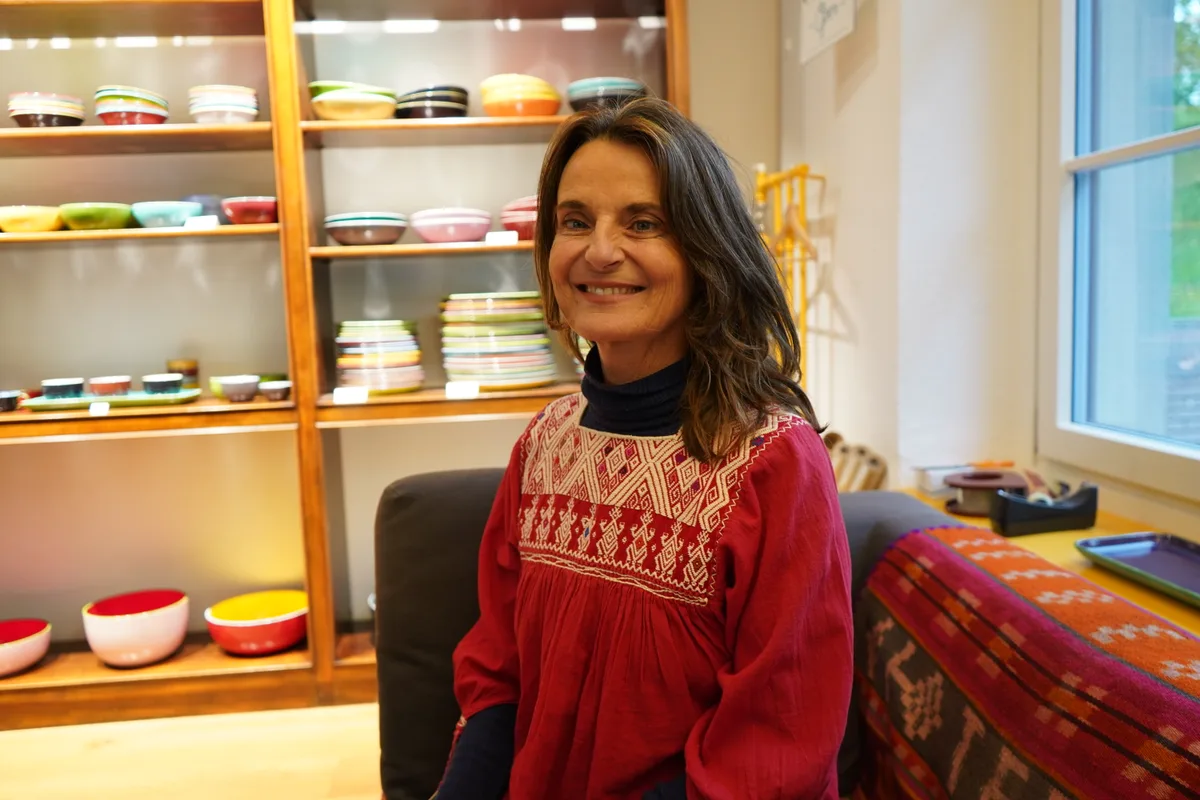 Nicolette Huhn sitzt vor einem Gestell mit Tellern in bunten Farben.